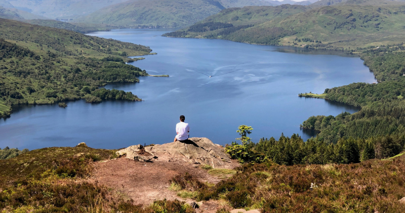 a person sitting on a rock overlooking a loch