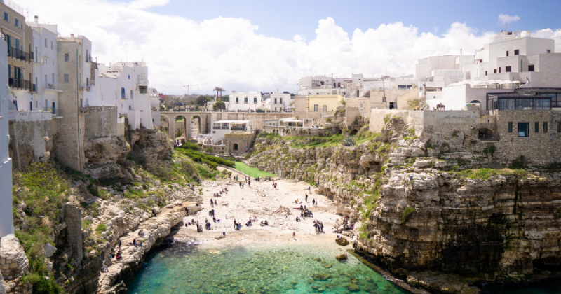 small bay with people standing on the beach and rocky outer edge