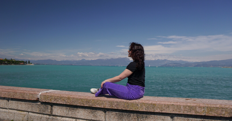 woman sat on a wall overlooking the blue sea in Italy