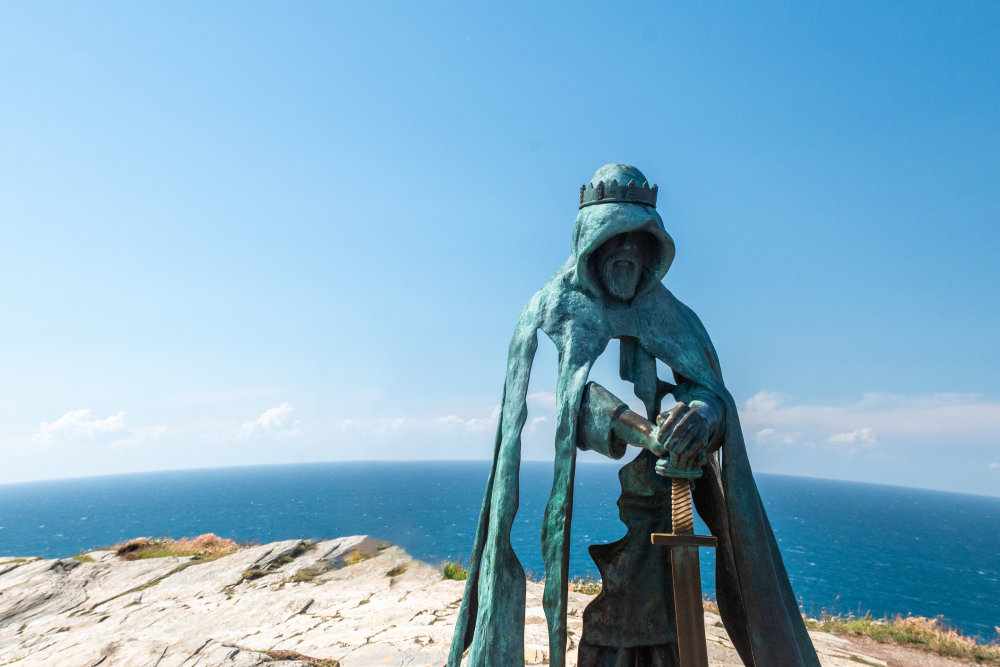king arthur statue overlooking bright blue sea