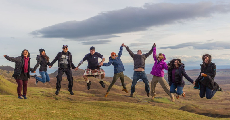 A group of people holding hands jumping in the air in nature