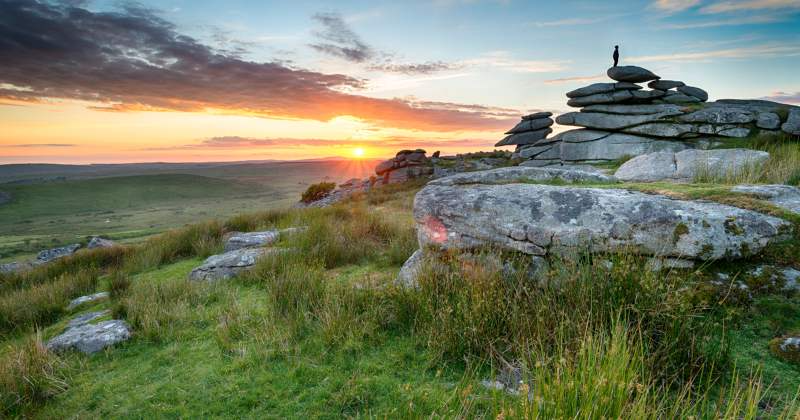 a collection of rocks stacked in bodmin moor with the sun setting in the background