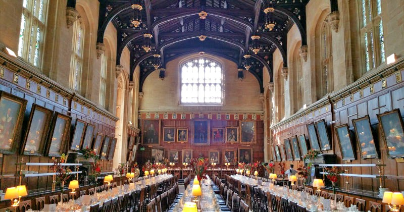 interior of a great hall lined with tables, chairs and lamps and the walls filled with paintings