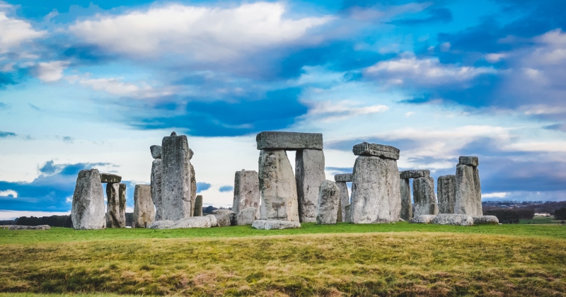 Stonehenge stands majestically against a backdrop of blue sky and clouds, surrounded by green fields.
