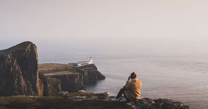 solo female looking out to a lighthouse on a rocky coastal cliff