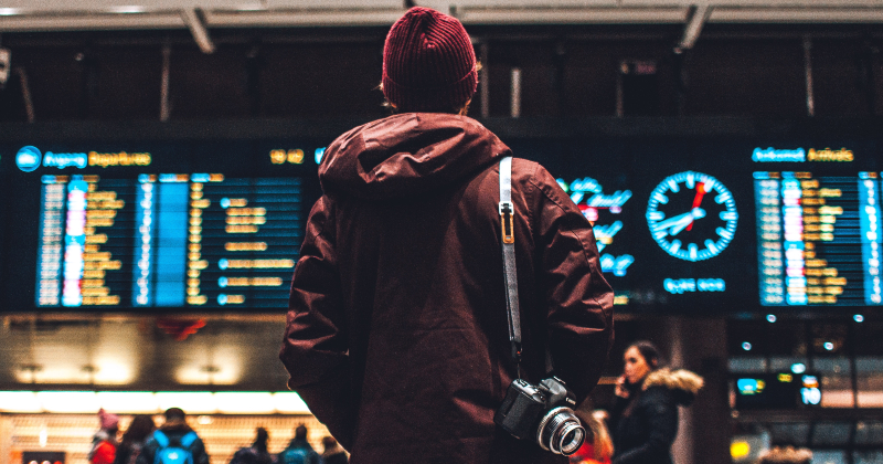 person with their back to the camera looking at a departures board in an airport