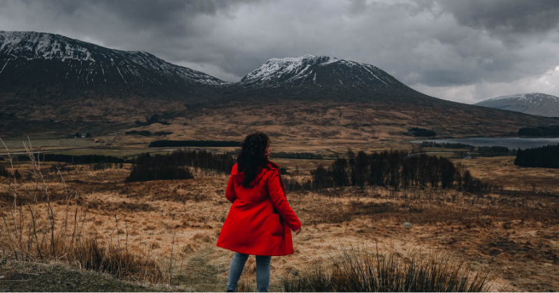 women wearing a bright red coast looking out to the Scottish mountain landscape
