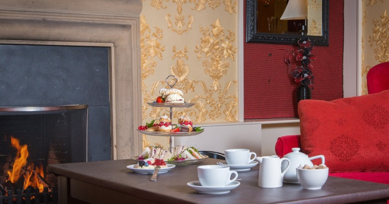 table with tea and scones on a platter lay in front of an open fire and next to a red sofa