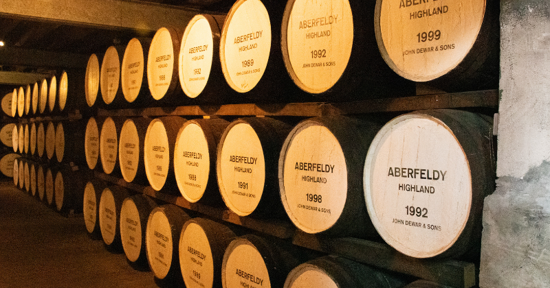 Rows of wooden barrels labeled "Aberfeldy Highland" with various vintage years displayed in a dimly lit cellar.