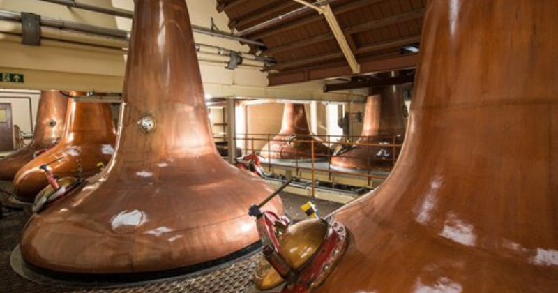 Interior of a distillery featuring large copper pot stills used in the whisky production process.