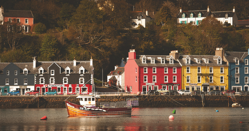 Colorful seaside buildings line the waterfront, with a boat anchored in front, creating a charming, picturesque scene.