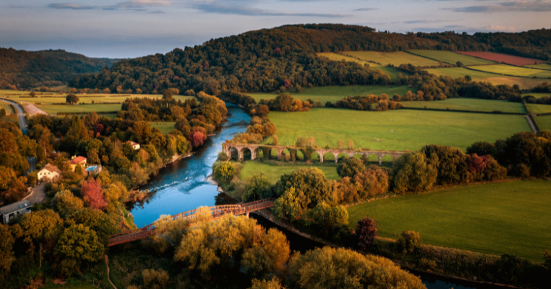 A scenic view of lush green hills, a winding river, and a historic bridge, showcasing the beauty of the UK landscape.