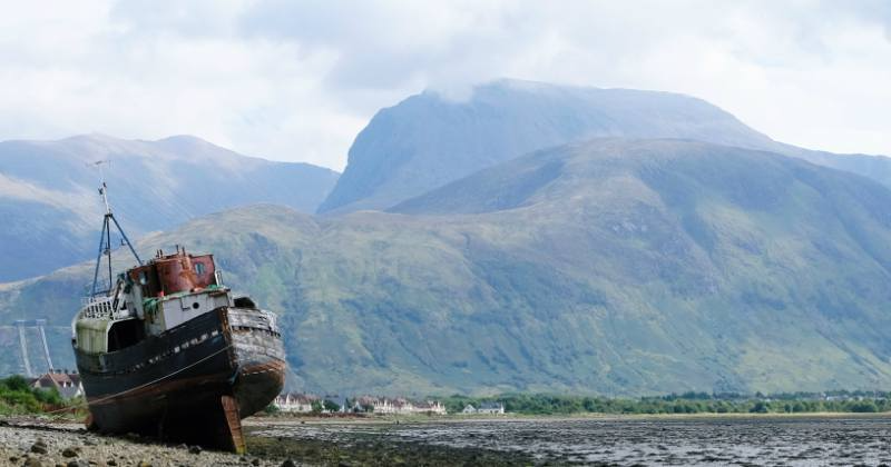 an old ship out of sea to the left with mountains in the background