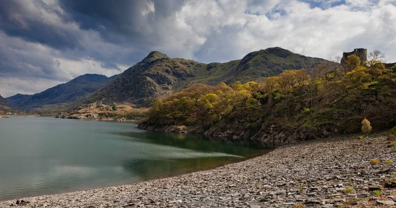 stoned beach in the foreground and mountains in the background with the lake to the left