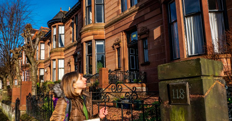 A woman looks up at elegant brownstone buildings while exploring the city, typical of small group tours offered by Rabbie's.