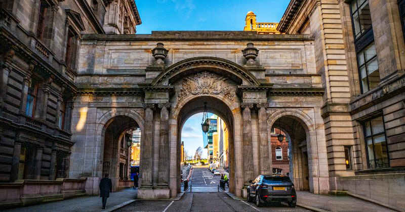 Historic archway in an urban setting, showcasing intricate stonework and leading to a bustling street in a city.
