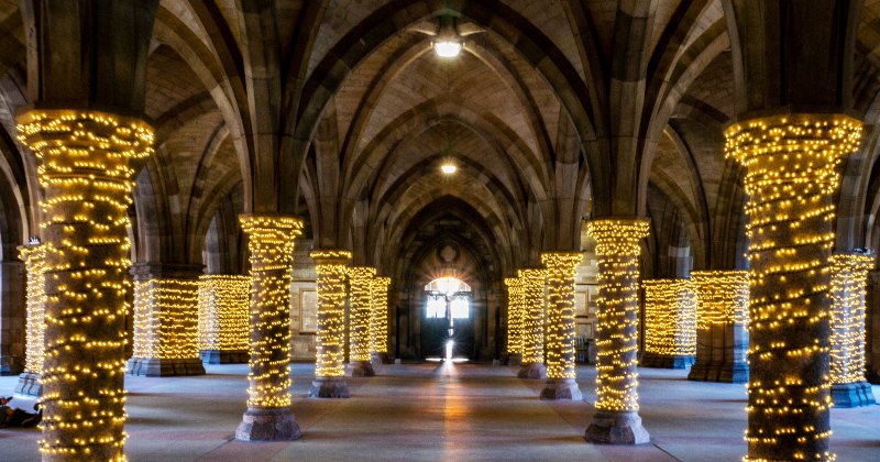 Illuminated stone arches with pillars wrapped in warm white lights, creating a magical atmosphere in a historic space.