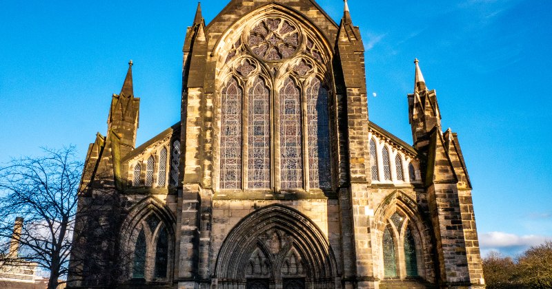 Historic church facade with intricate architecture and stained glass, set against a clear blue sky.