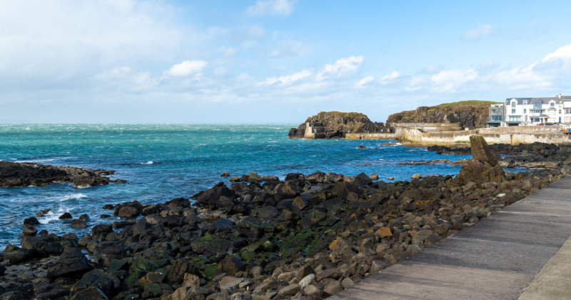 Rocky shoreline with turquoise waters and a coastal path, under a bright sky, showcasing the beauty of the UK coast.