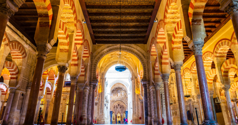 Interior of a historic building featuring columns and arches with red and white stripes, highlighting beautiful architectural details.
