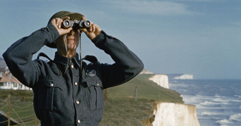 a man in uniform looking through binoculars by the cliffs