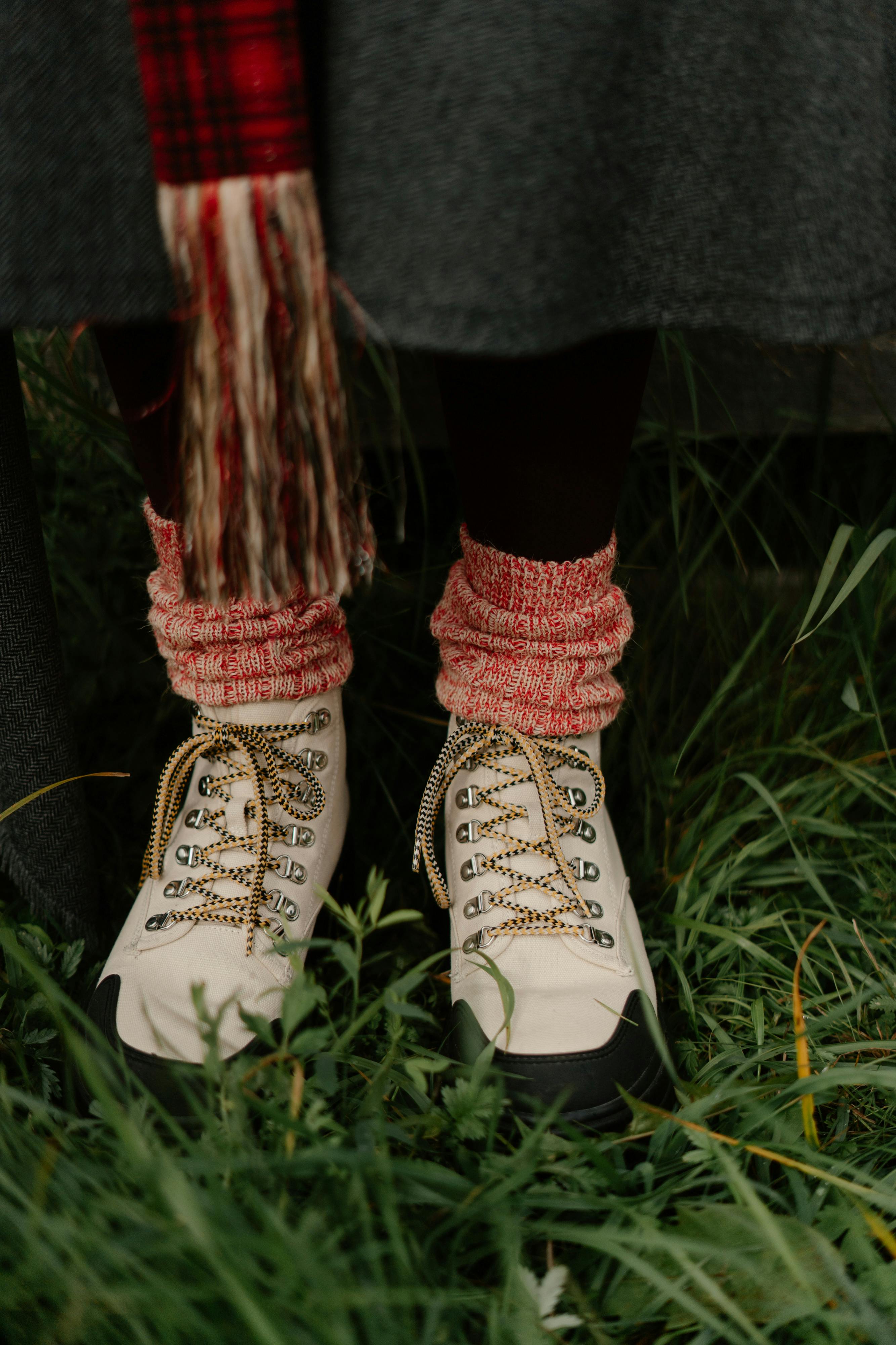 A close-up of white hiking boots with colorful knitted socks, set against a grassy background, conveying outdoor adventure vibes.
