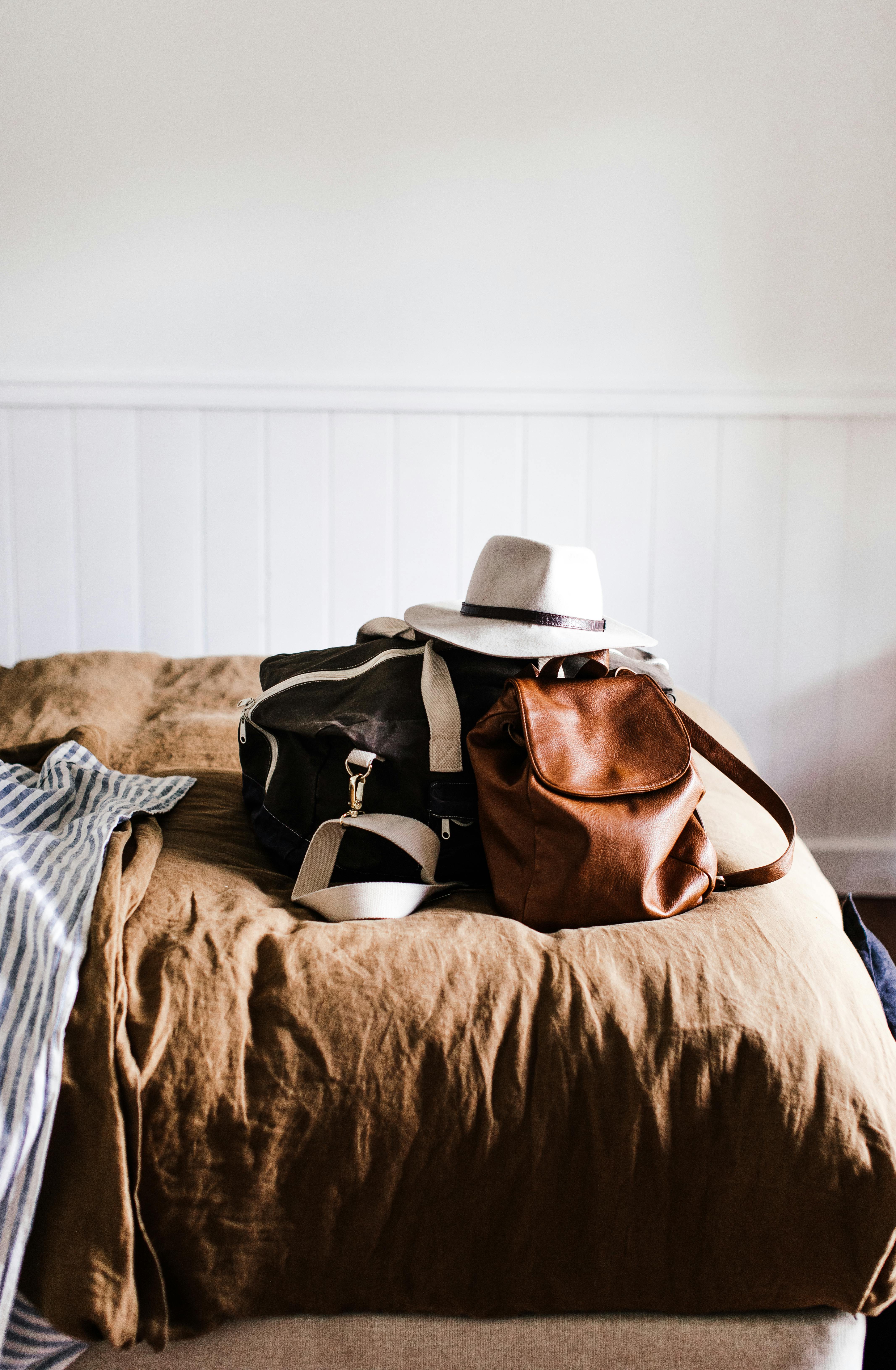 A travel scene featuring a duffel bag, a leather backpack, and a hat on a bed, perfect for a UK adventure.