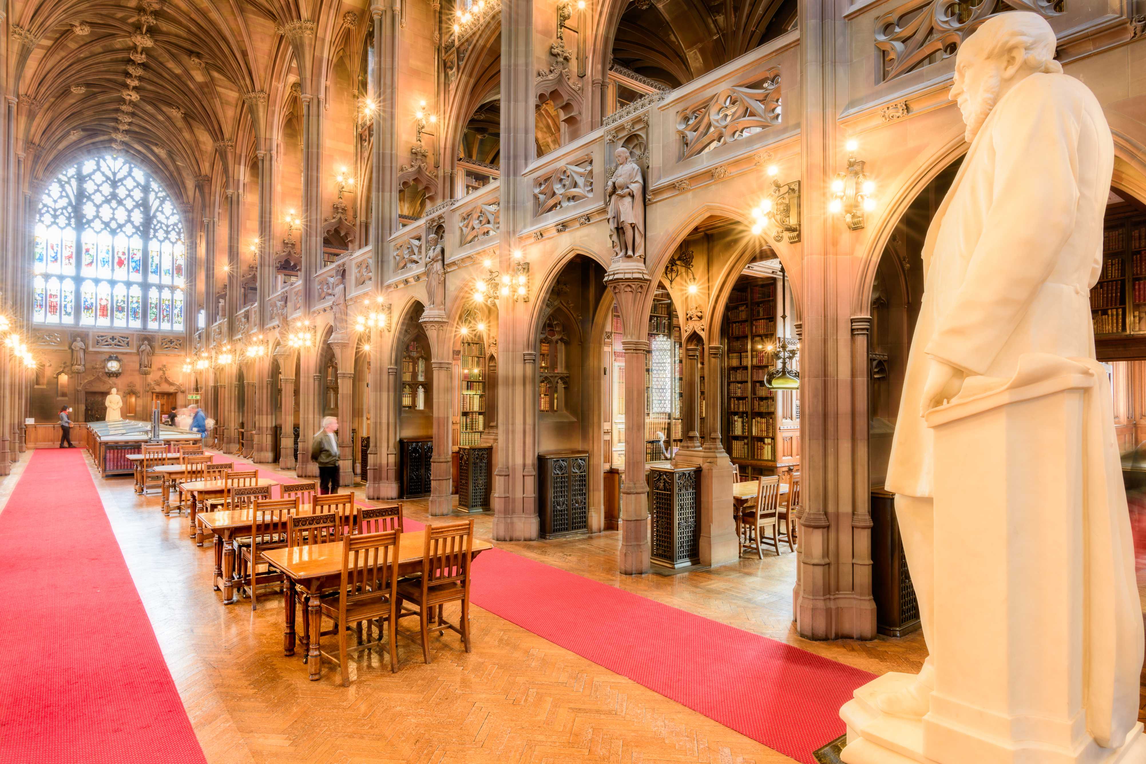 A grand, historic library with wooden tables, arched ceilings, warm lighting, and a prominent statue, inviting exploration.